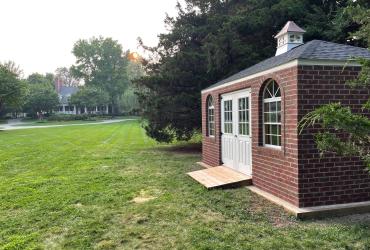 a side view of the brick hip-roof shed on a lush green lawn.