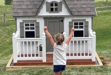 a young girl runs up to her playhouse with both hands in the air in excitement