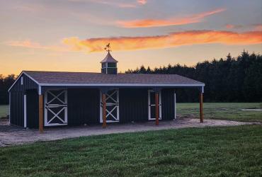 row shed for horses with sunset behind it