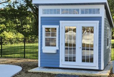 front view of a light blue studio shed next to a pool.