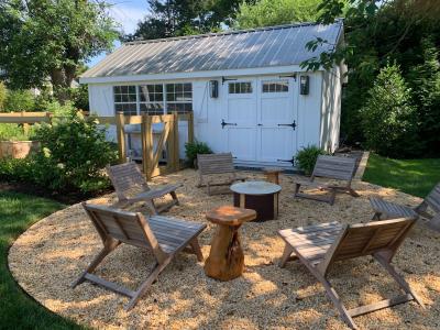 Backyard she shed in white siding with fireplace and seating in front