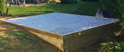 Crushed gravel foundation for shed surrounded by treated wood retaining wall.